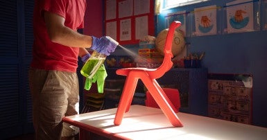 Man in red shirt  and blue gloves sprays cleaner on red children's chair